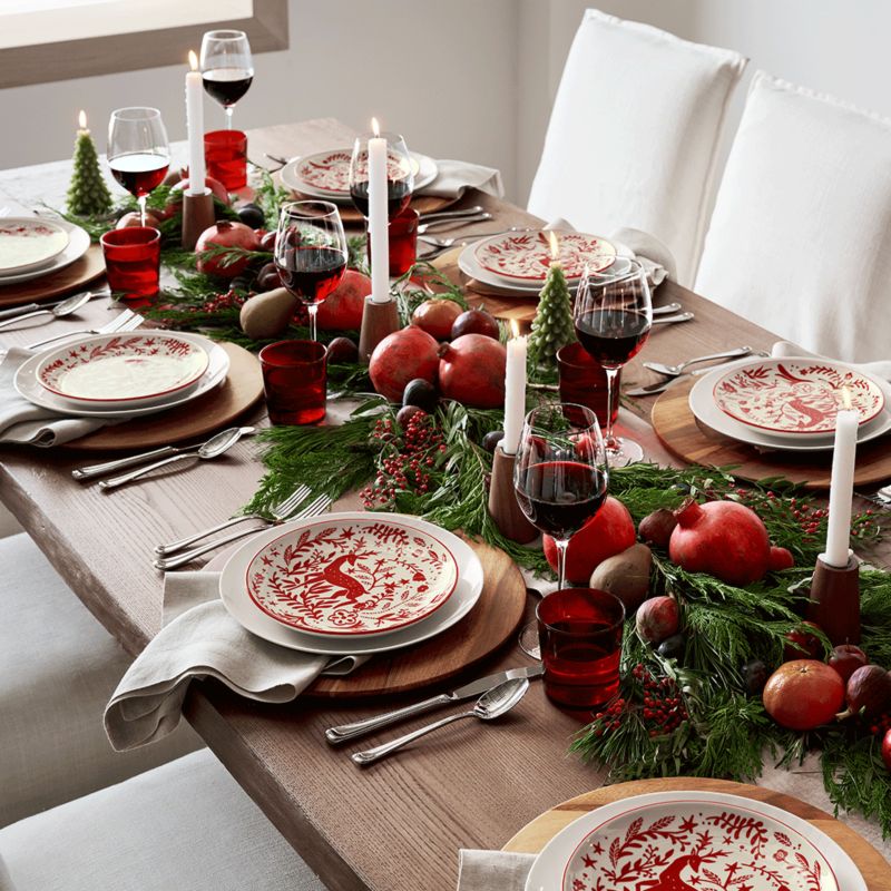 Wood table set with red and white reindeer plates, red glasses, white candlesticks, and greenery from our holiday decor updates guide.