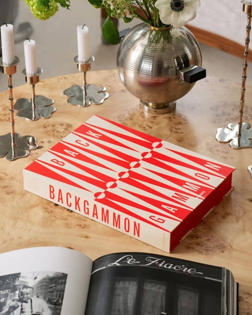 Red and white backgammon set on a table with an open book and a candle from our home decor gift guide.
