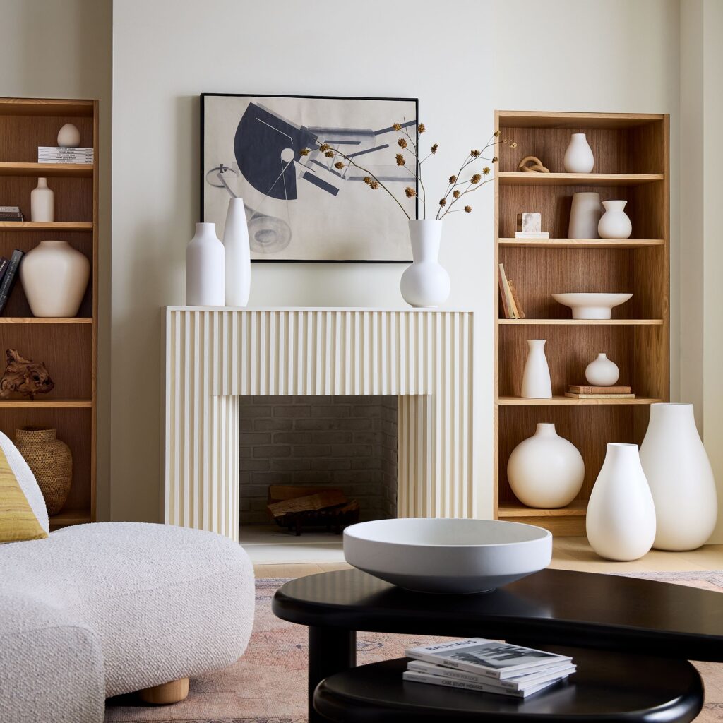 Living room with black coffee table, white boucle curved sofa, and white ceramic vases scattered on the floor and shelving.