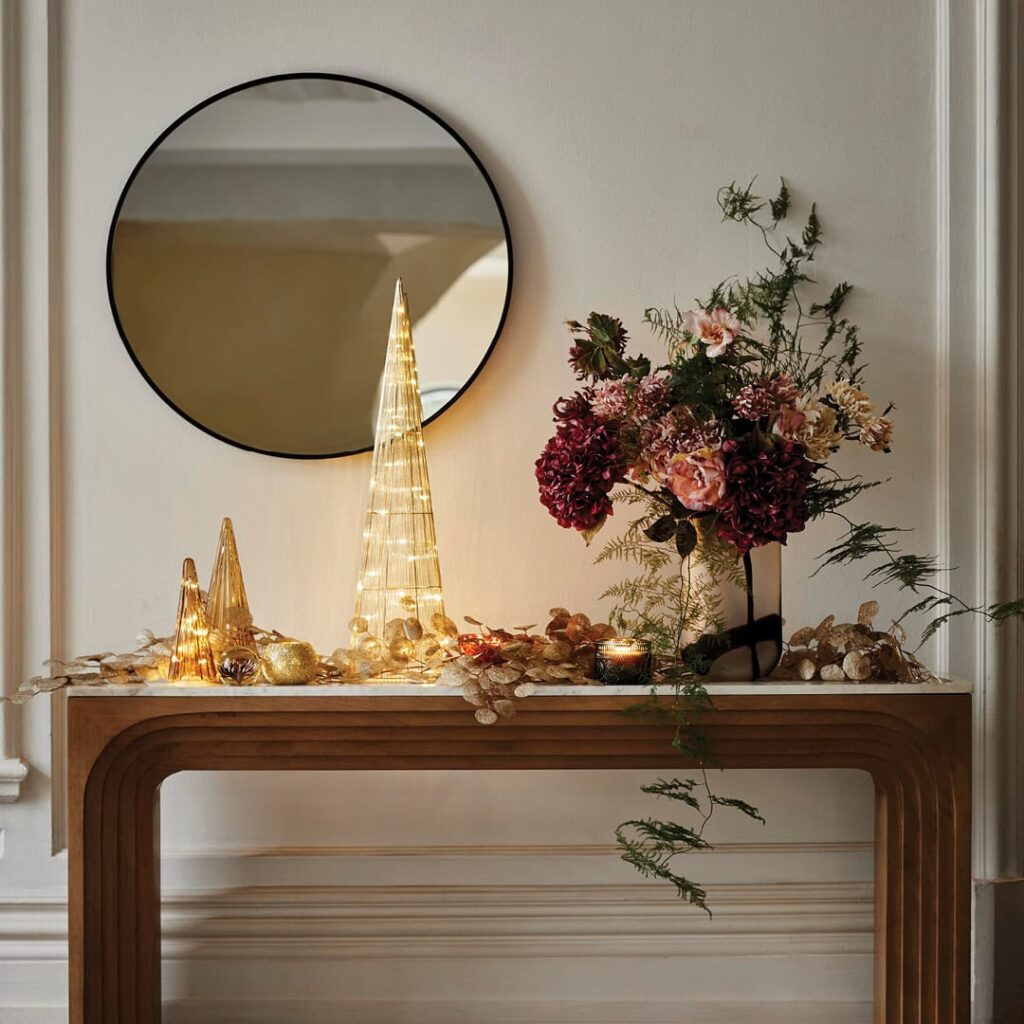 Entryway console decorated for the holidays with lighted decor and red and pink flowers.