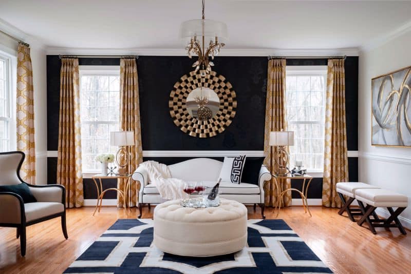 Living room with black accent wall, gold mirror, black and white rug, and white upholstered furniture.