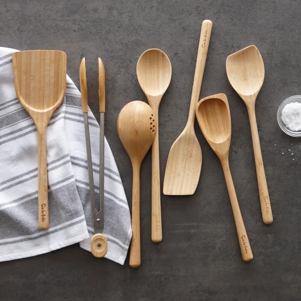 Sue la Table bamboo utensils on a gray countertop and a gray and white kitchen towel.