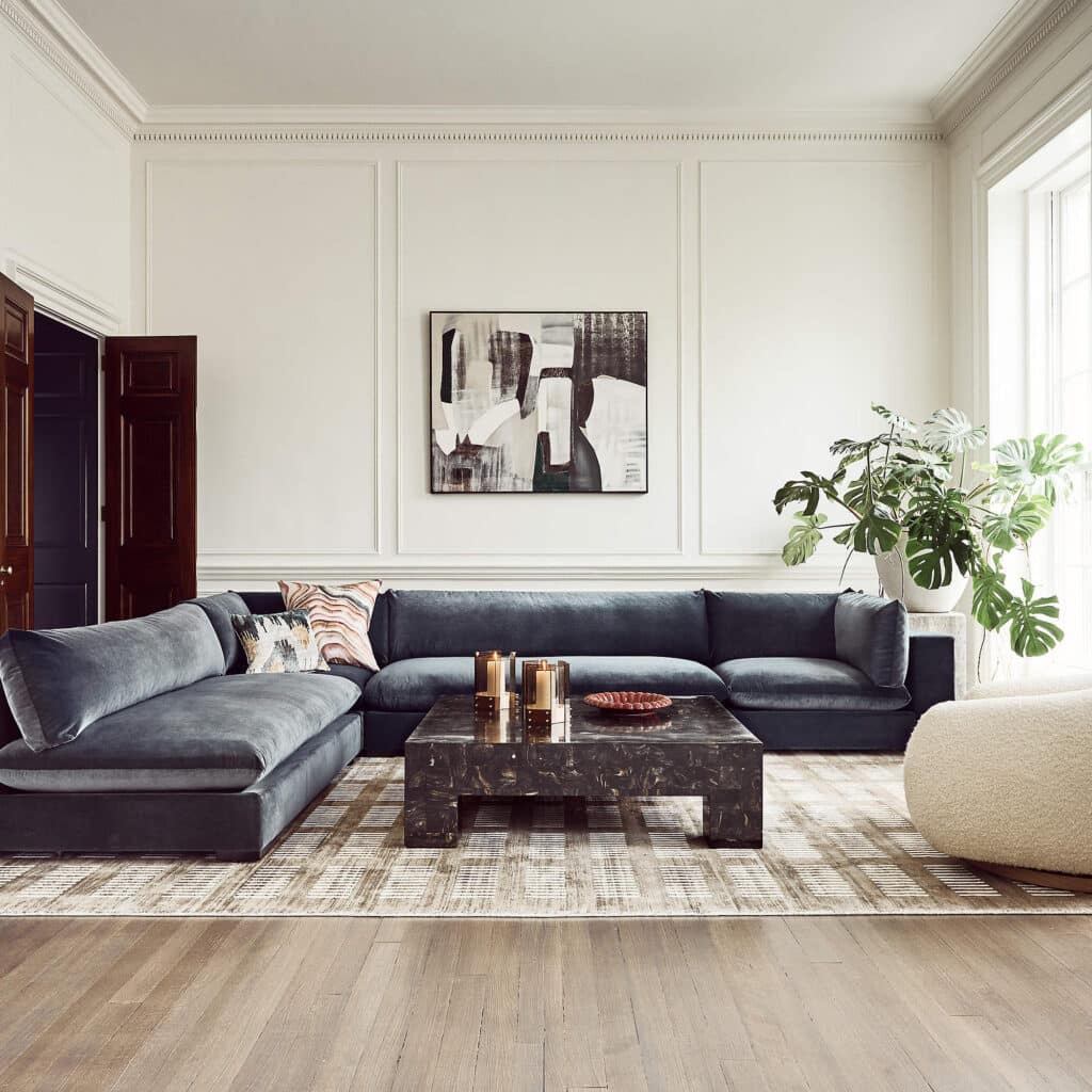 Square marble coffee table properly scaled in front of a charcoal velvet sectional with clear circulation space.