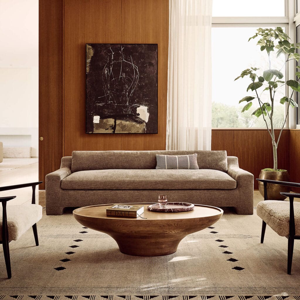 Inverted oval wood coffee table proportioned correctly in front of a taupe velvet sofa with clear circulation space.