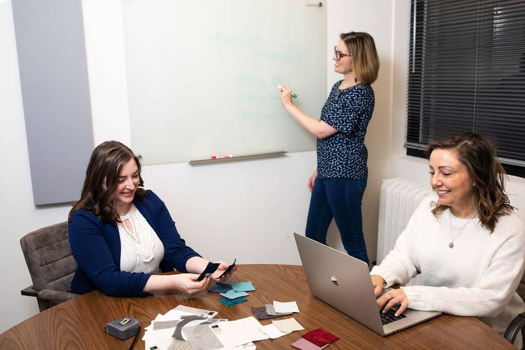 Interior designer Betsy Helmuth reviewing a living room layout with two designers during a planning discussion.