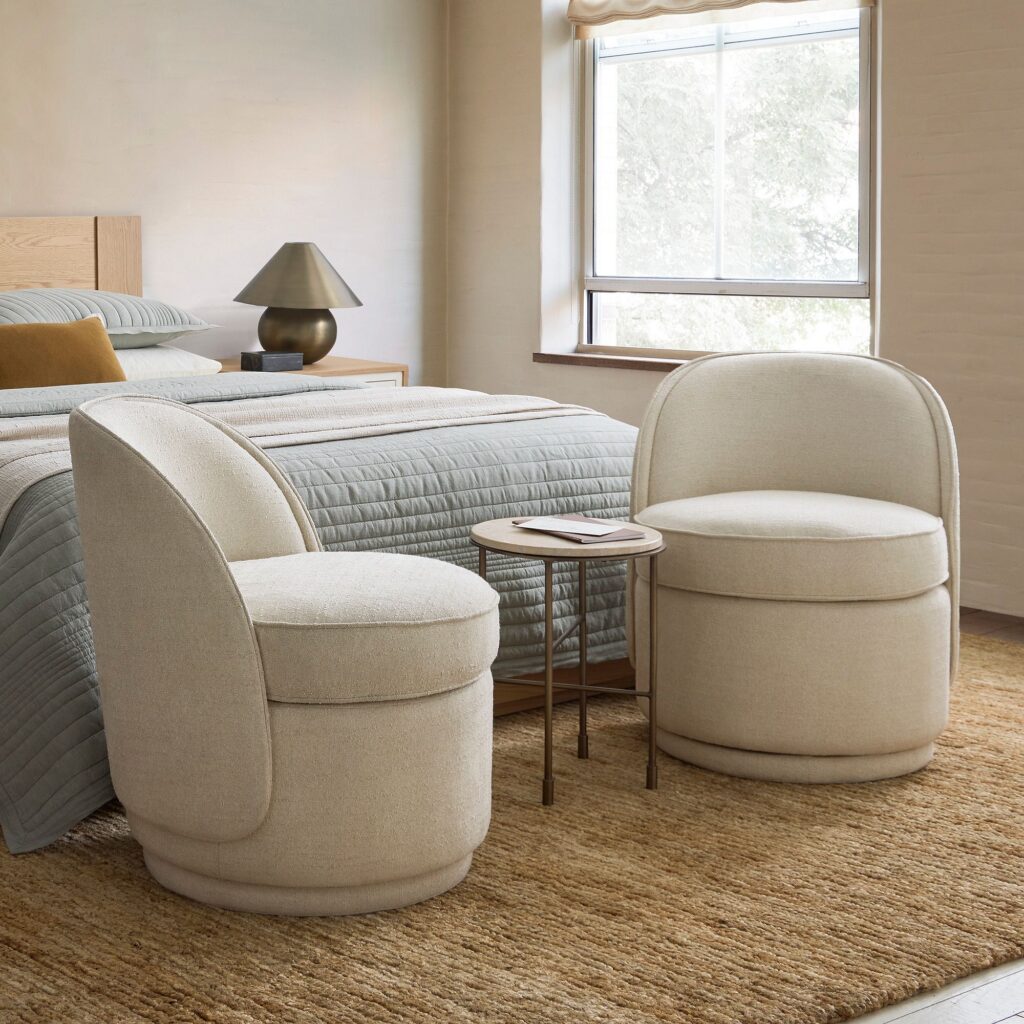 Neutral upholstered accent chair layered into a calm bedroom with textured pillows and soft lighting.