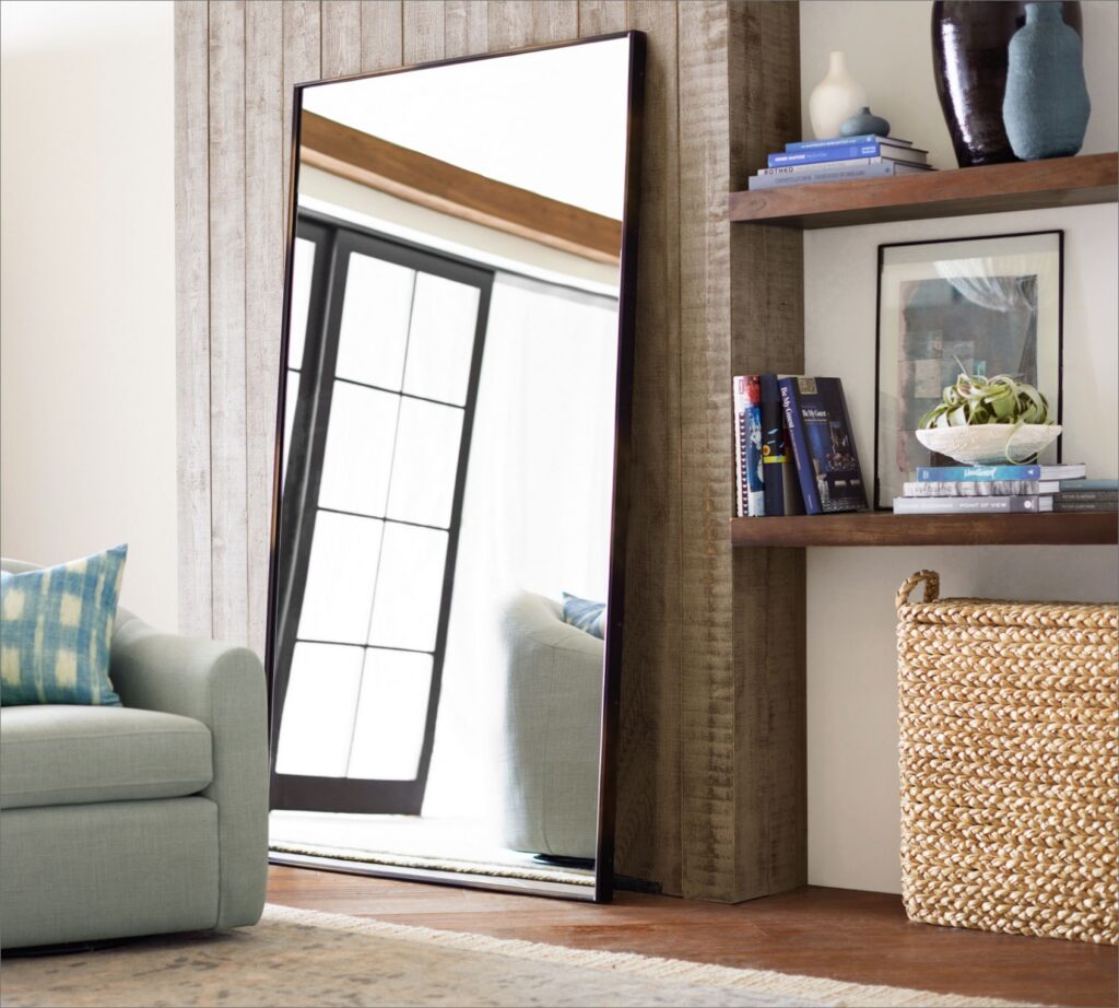 Large leaning mirror placed opposite a window in a bright living room.