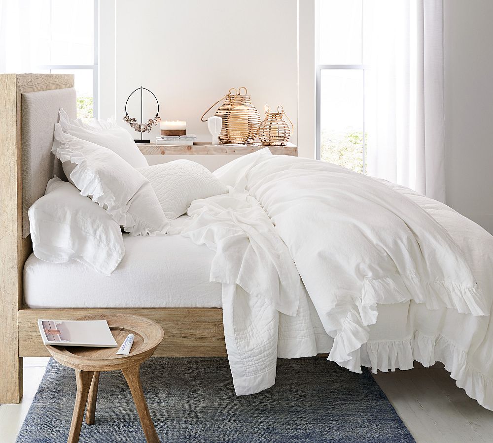 White linen summer bedding layered with lightweight neutral pillows and a textured quilt.