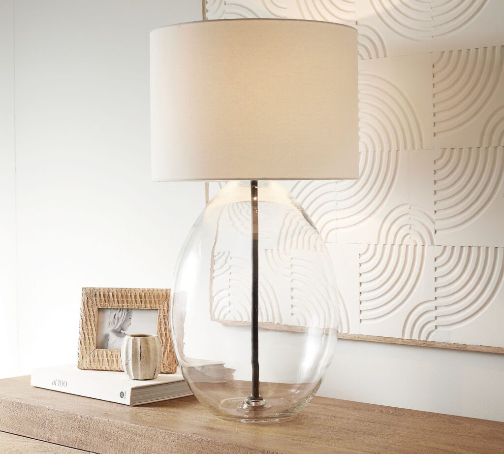 Glass base table lamp styled on a side table in a neutral living room.